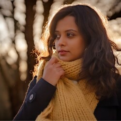 Gunjan Menon in knitted tan-coloured scarf and black jacket with trees and sunset/sunrise in background