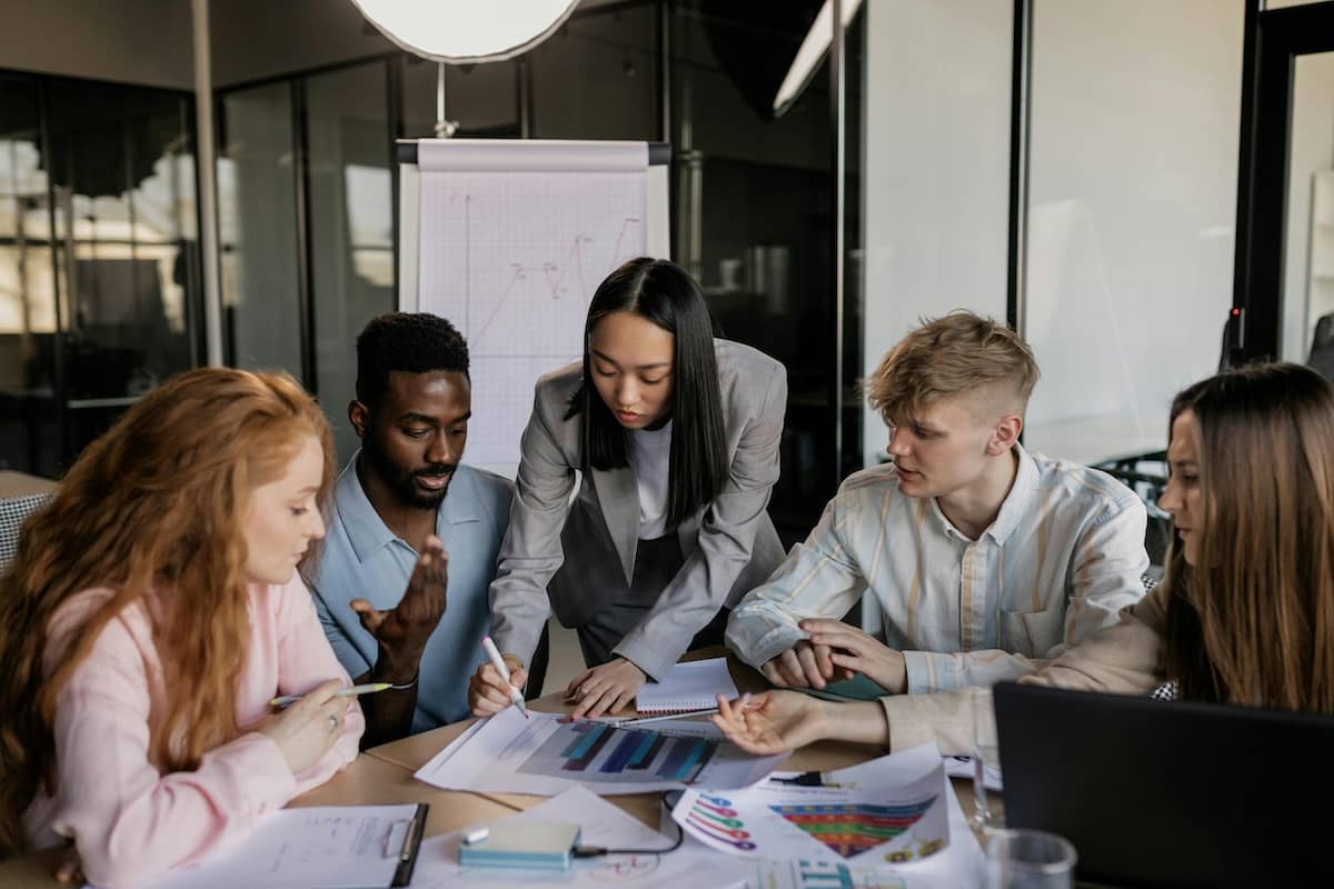 Stock image of staff in professional attire around a desk covered in documents, deep in discussion