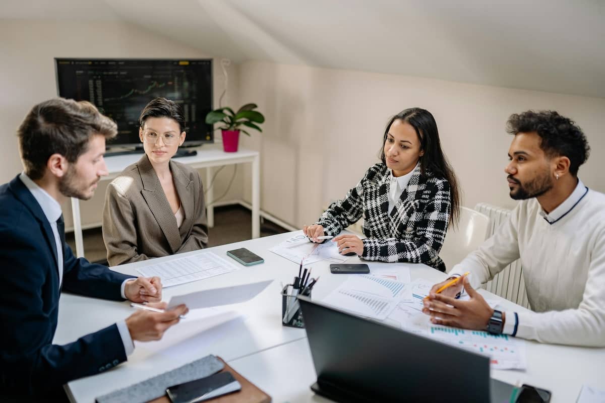 Stock image of staff in professional attire around a desk covered in documents, deep in discussion