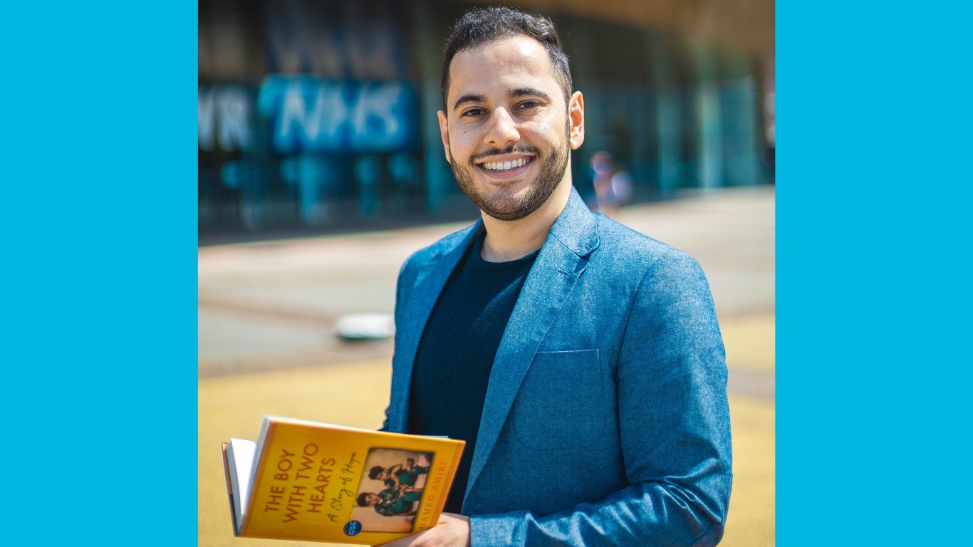 Hamed Amiri smiling holding his book The Boy with Two Hearts.