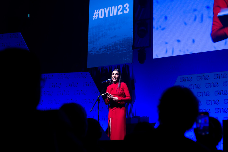 Canadian poet, Rupi Kaur wearing red suit presenting on stage at Belfast One Young World Summit 2023