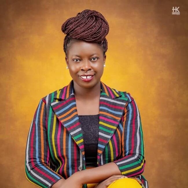 Adenike Oladosu portrait wearing striped colourful jacket against brown yellow background