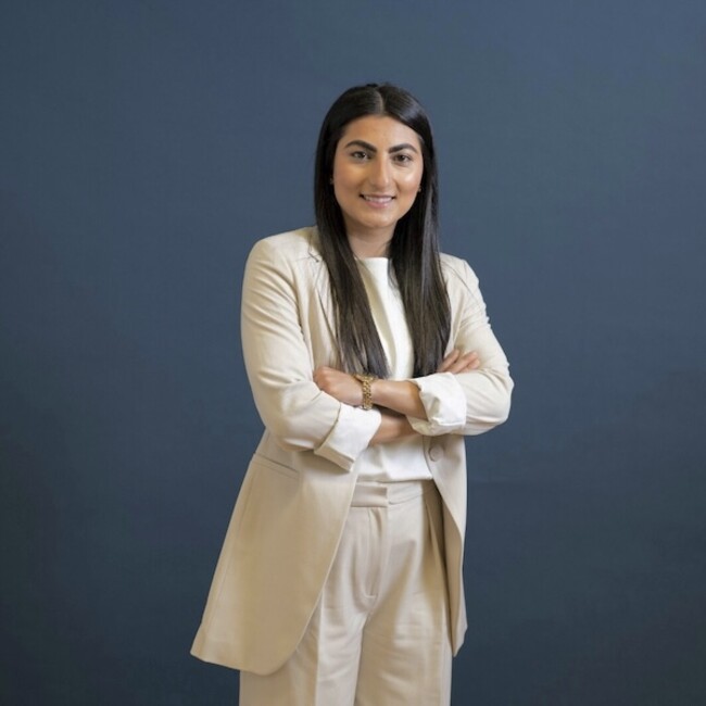 Farkhunda Muhtaj portrait photo wearing long beige overcoat against dark blue background