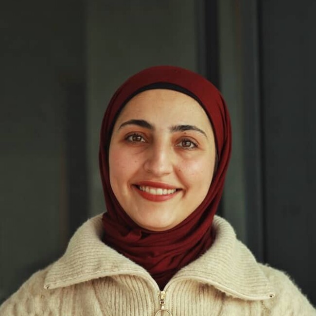 Lama Amro in maroon headscarf against dark green background