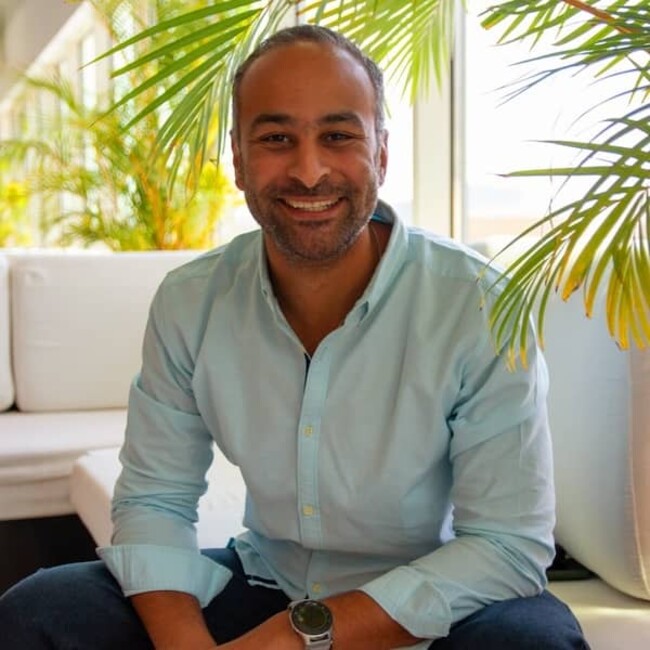 Seif Taher en chemise décontractée vert clair sur fond de canapé blanc et de plantes d'intérieur