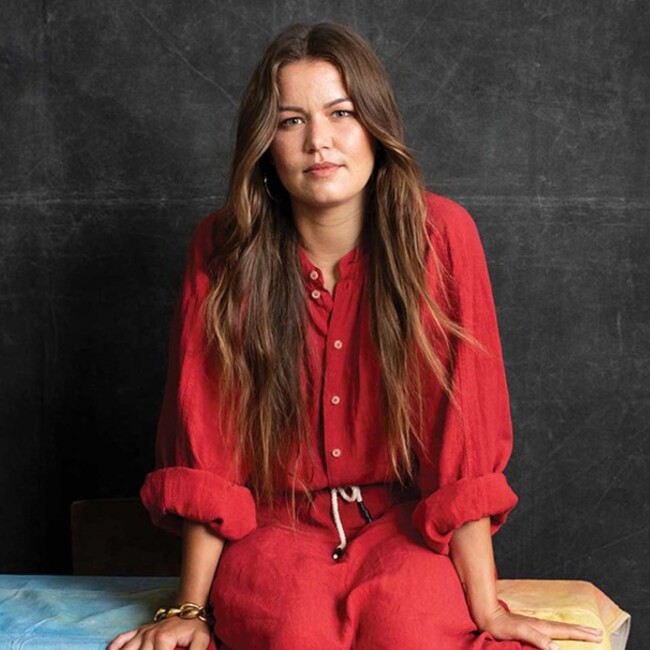 Portrait of Vanessa Turnbull-Roberts in red dress sitting down against black background