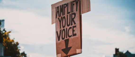 Picture of a placard with "Amplify Your Voice" written in black pen